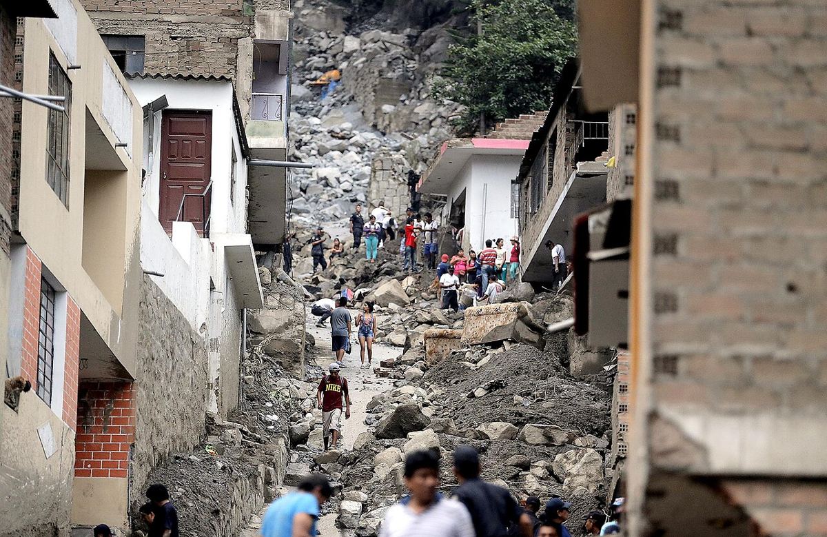 Pobladores caminando entre rocas y escombros que dejó una avenida de lodo en una quebrada